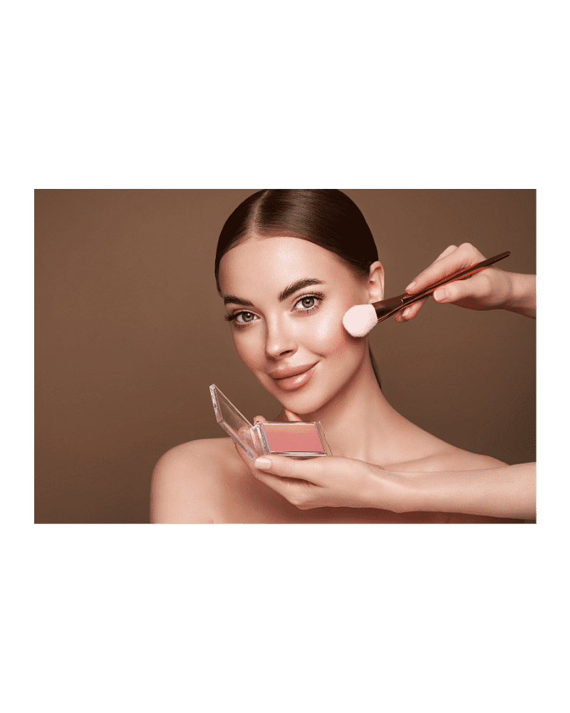 Woman applying blush with a makeup brush, holding a compact, against a brown background.