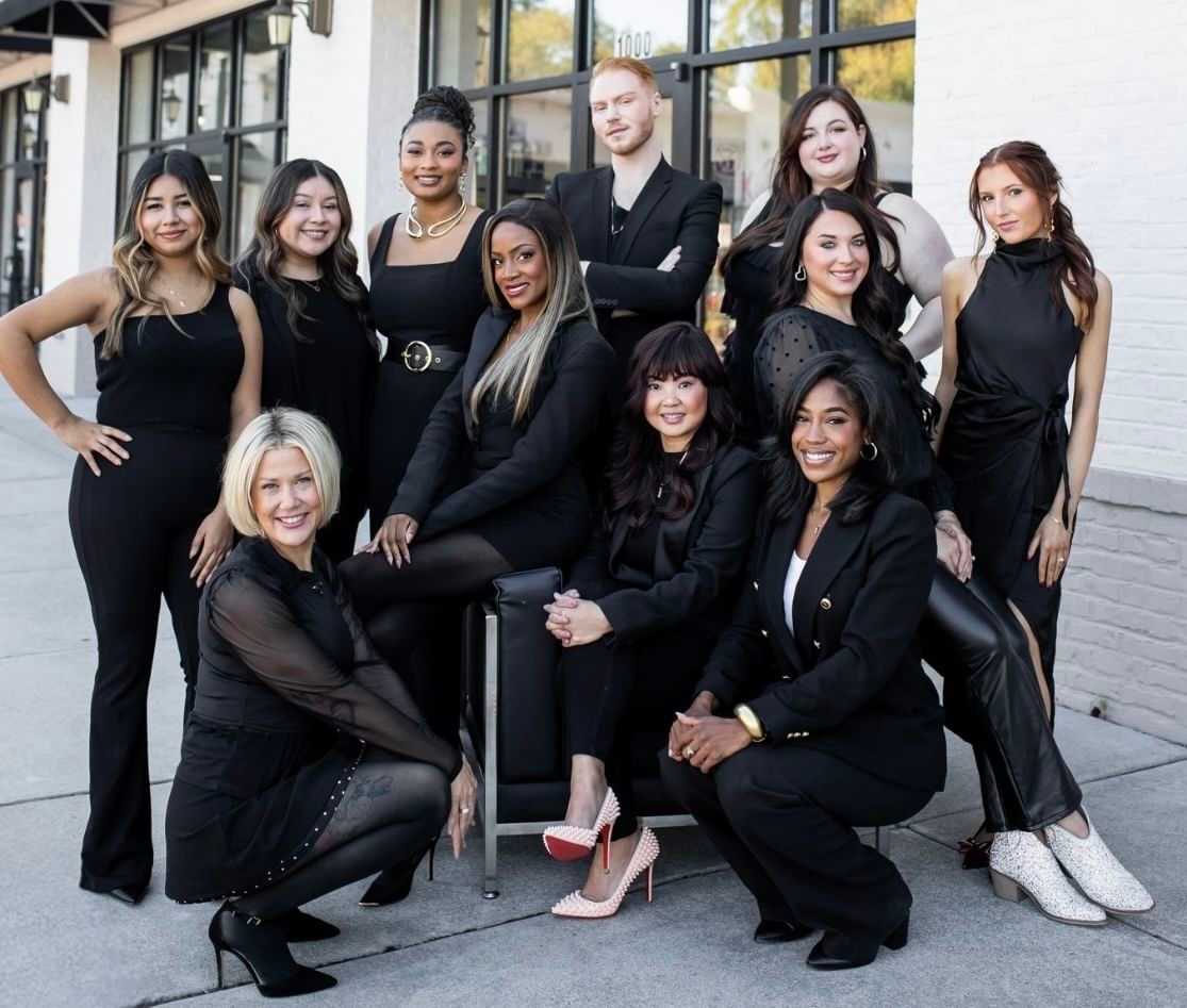 A diverse group of 10 people posing together outside a building, all dressed in black outfits.